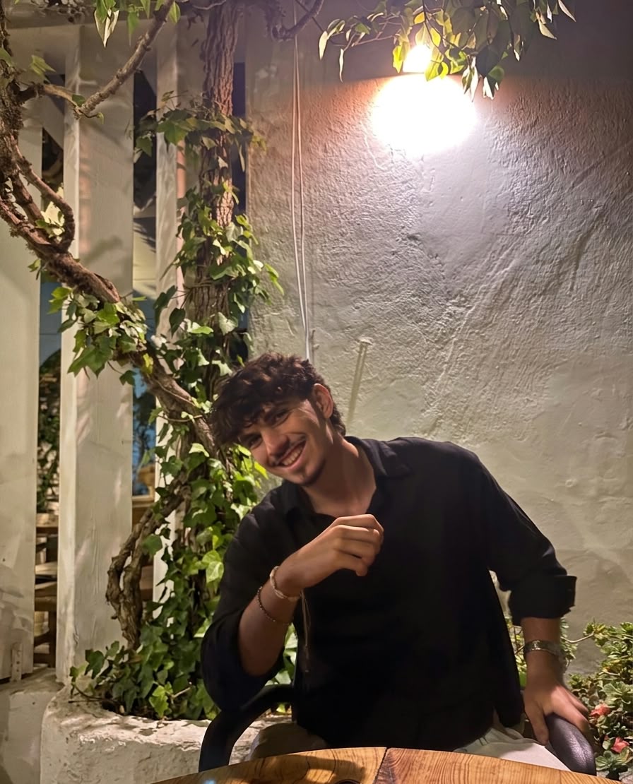 Gürkan Vatansever smiling at a table under a vine-covered pergola