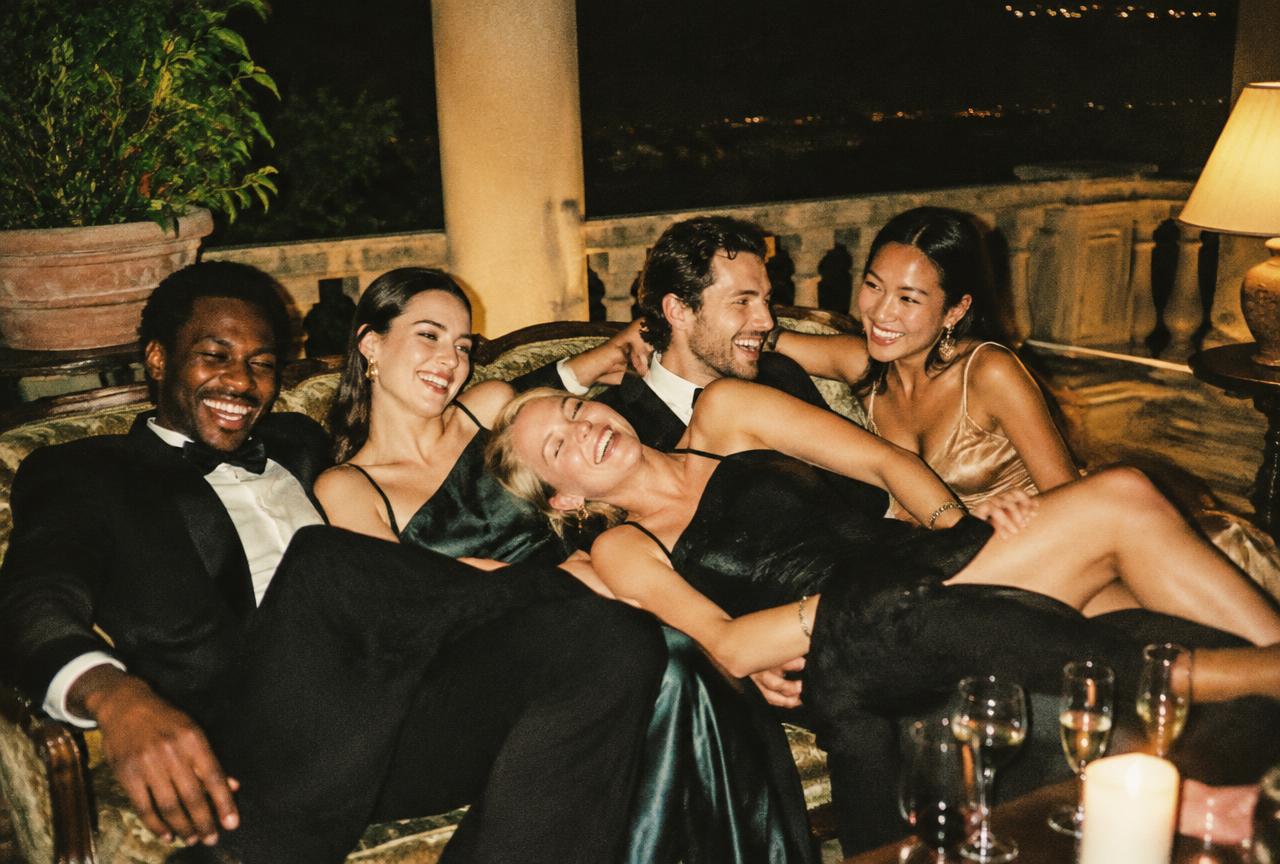 Friends in evening wear laughing together on a sofa